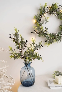 Christmas wreath with artificial berries and pine branches near a blue glass vase