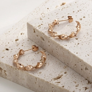 Macro view of rose gold twisted hoop earrings on a natural travertine stone surface