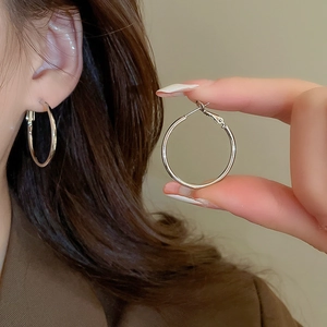 Detailed view of polished silver hoop earrings shown on a model and held for size scale