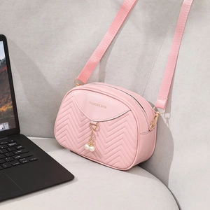 Pink shell crossbody bag with pearl pendant and V-shaped quilting on gray sofa