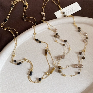 Detail of layered vintage tiger eye beaded necklace with gold chain and pearls on tray