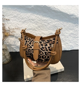 Detail of leopard print hobo bag with brown leather patchwork and metallic buckle on books