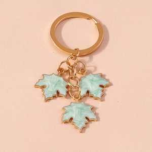 Fashionable gold key ring featuring three light green maple leaf enamel pendants on pink background