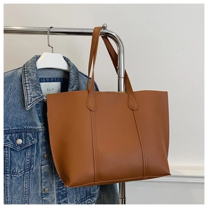 Grand sac cabas marron en cuir avec coutures verticales suspendu devant une veste