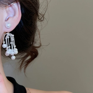 Close-up of pearl tassel drop earrings with silver metal chains on female model