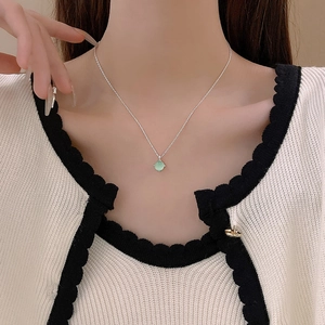 Detail of silver chain with light green round gemstone pendant worn on neck