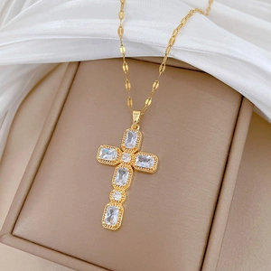 Luxueux collier croix en titane doré avec strass carrés sur une boîte à bijoux beige