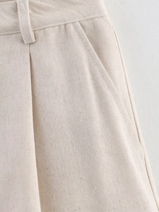 Detail of beige linen shorts featuring waist pleats and natural fabric texture