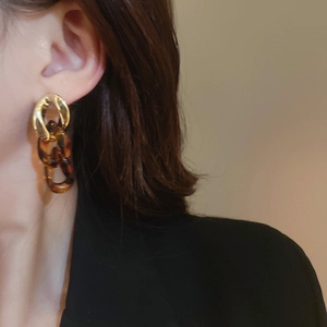 Close-up of golden metal and tortoiseshell acrylic link earrings worn by a model