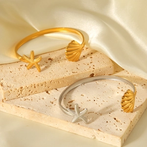 Starfish and seashell open bangle in gold and silver finish on a neutral satin background