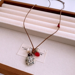 Détail d'un pendentif cœur en pierre vintage avec fleur en métal sur cordon tressé