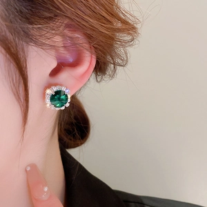 Nahaufnahme eleganter smaragdgrüner Ohrstecker mit Diamantumrandung am Modell