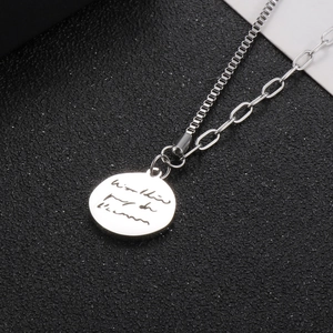 Macro detail of silver round pendant necklace with engraved script and mixed link chain