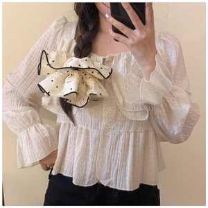 Detail of cream shirt featuring polka dot bow tie and ruffled chiffon textures