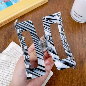 Large vintage zebra stripe hair claw clip on wooden desk background with lifestyle items