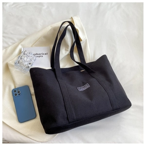 Top-down view of black canvas tote bag with fashion label and lifestyle accessories