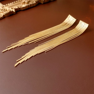Detail view of long golden chain tassel earrings on a textured leather surface background