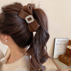 Detail of brown velvet bow hair clip with diamond buckle on brunette ponytail