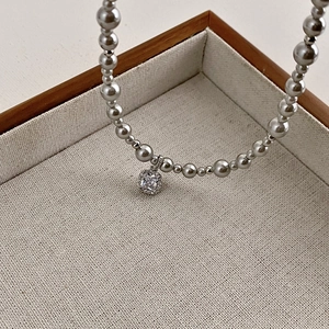 Detail of grey pearl necklace with square crystal pendant on beige display stand