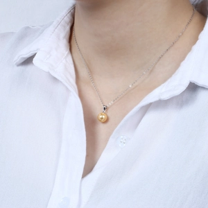 Close-up of a minimalist necklace featuring a golden shell pearl pendant on a silver chain
