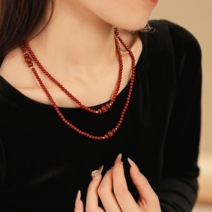 Dettaglio di collana a doppio strato di perle rosso scuro con accenti dorati su nero