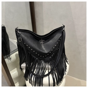 Detail of black crossbody bag with silver rivets, fringe, and metal cross charms
