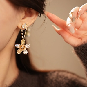 Detailed close-up of a golden flower drop earring with pearls and clear zircons on model