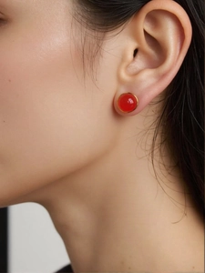 Detail shot of a round red jasper earring with gold frame worn by a model