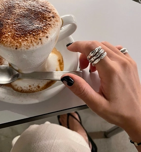 Close-up of multilayer wavy silver rings and a smooth solid band with metallic texture