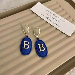Detail view of Klein blue oval earrings with gold letter B on a beige tray