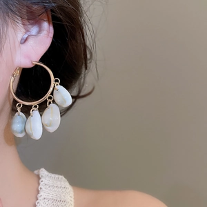 Detailed close-up of golden hoop earrings featuring natural white shell pendants on model