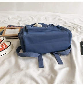 Blue canvas backpack with cute plush charm and badges on white fabric background