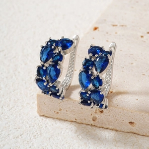 Macro shot of silver hoops with pear-cut deep blue gemstones on stone surface