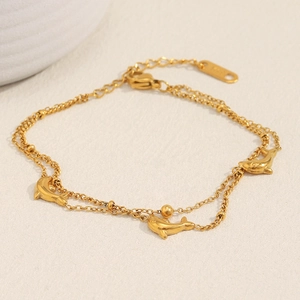 Detail view of 18K gold plated double layer dolphin pendant chain bracelet on beige surface