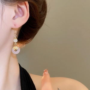 Détail de boucles d'oreilles donut en calcédoine rose avec glands dorés sur modèle