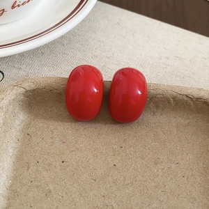Detailed macro shot of red oval teardrop earrings with high gloss enamel finish on beige linen