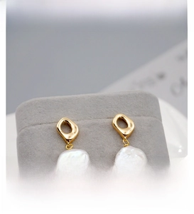 Detailed close-up of Baroque pearl earrings with golden metal hooks on grey velvet