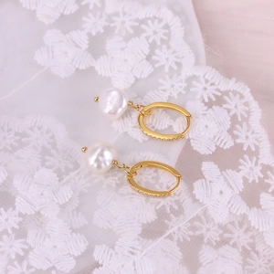 Close-up of baroque pearl earrings with gold pave zircon hoops on white lace background