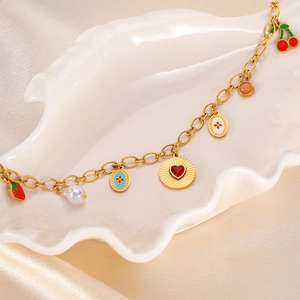 Detail of golden charm necklace with red strawberry, cherry, heart, and pearl pendants