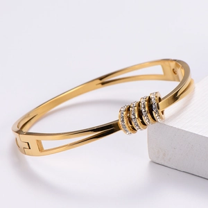 Elegant gold titanium bangle with five crystal-encrusted rings on a textured wooden block
