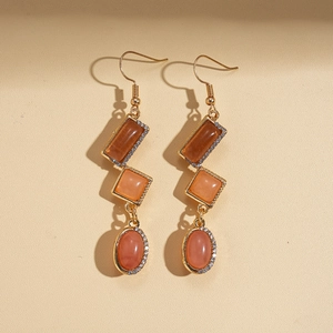 Close-up of geometric drop earrings with amber resin and rhinestones in gold finish