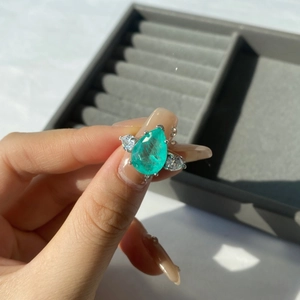 Macro shot of a pear-cut emerald silver ring held over a grey jewelry tray