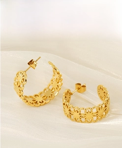 Detail of geometric cutout gold earrings on white silk fabric with polished finish