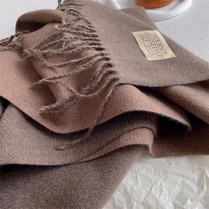 Detailed macro view of soft brown cashmere scarf with fringe edges and brand textile label