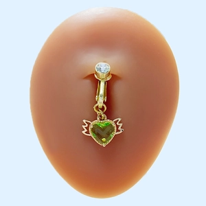 Détail d'un piercing de nombril doré avec cœur vert et ailes sur un mannequin