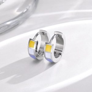 Close-up of silver steel hoop earrings with yellow, white, and purple enamel geometric blocks