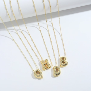 Gold letter pendants with clear zircons on bead chains over a white background