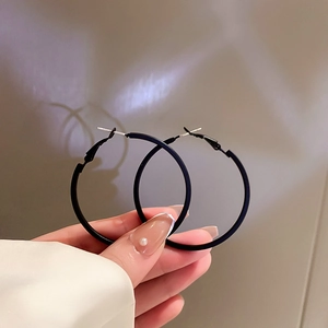 Close-up of matte black hoop earrings held by hand showing smooth texture and large design