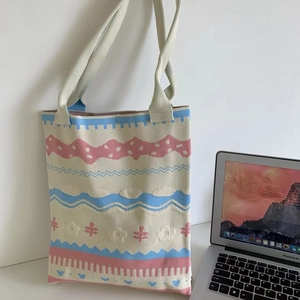 Detail of knitted tote bag with blue and pink patterns next to a laptop on desk