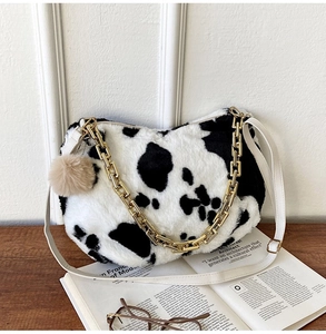 Detail of cow print faux fur tote bag with gold chain strap on a wooden desk